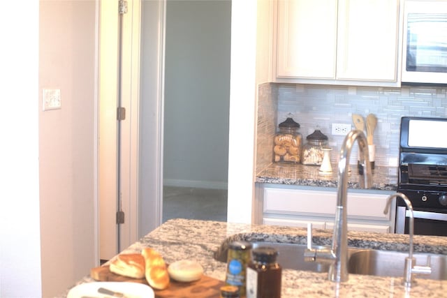 kitchen featuring white cabinets, light stone countertops, and backsplash