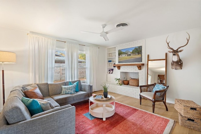 living room featuring a brick fireplace, hardwood / wood-style floors, ceiling fan, and built in shelves