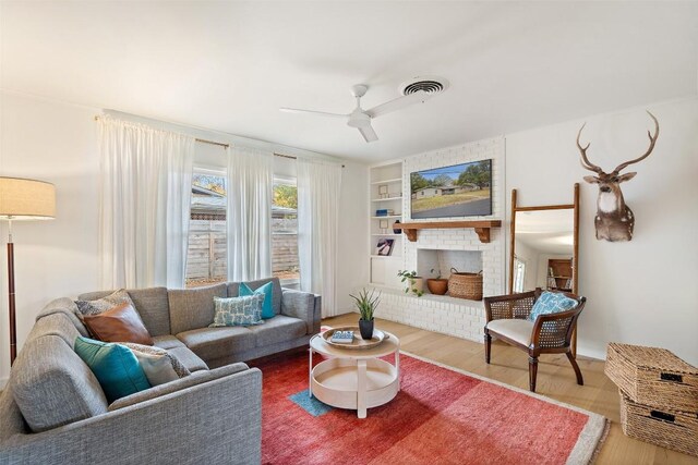 living room featuring a brick fireplace, hardwood / wood-style flooring, built in shelves, and ceiling fan