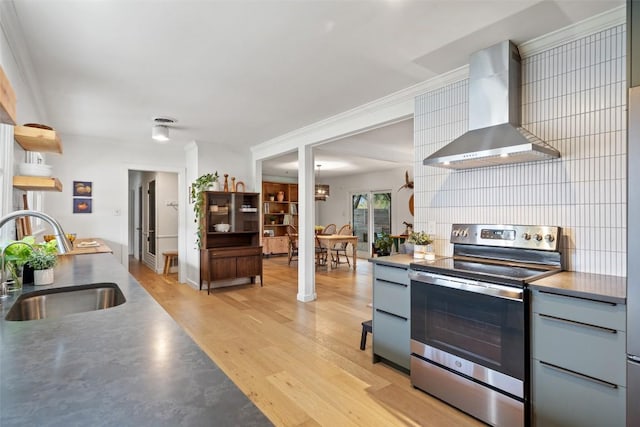 kitchen with light wood finished floors, decorative backsplash, wall chimney exhaust hood, stainless steel electric stove, and a sink