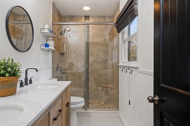 full bathroom with double vanity, toilet, a stall shower, wainscoting, and a sink