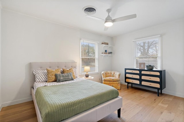 bedroom with a ceiling fan, visible vents, baseboards, and wood finished floors