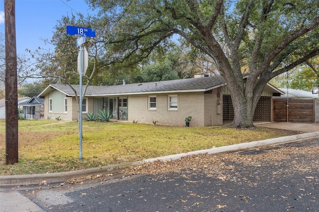 ranch-style home featuring driveway, a chimney, a front lawn, and brick siding