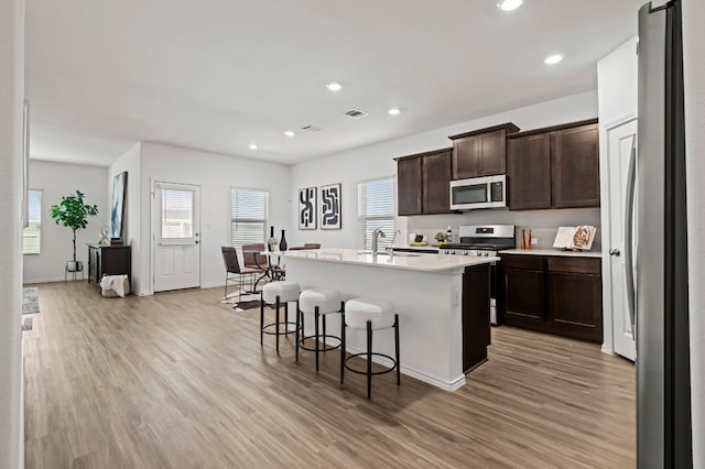 kitchen featuring a breakfast bar area, appliances with stainless steel finishes, dark brown cabinets, light hardwood / wood-style floors, and an island with sink