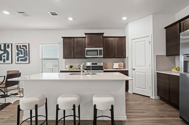 kitchen featuring sink, stainless steel appliances, dark hardwood / wood-style floors, dark brown cabinetry, and a center island with sink