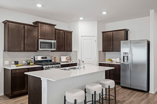 kitchen featuring sink, appliances with stainless steel finishes, a kitchen island with sink, dark brown cabinetry, and light wood-type flooring