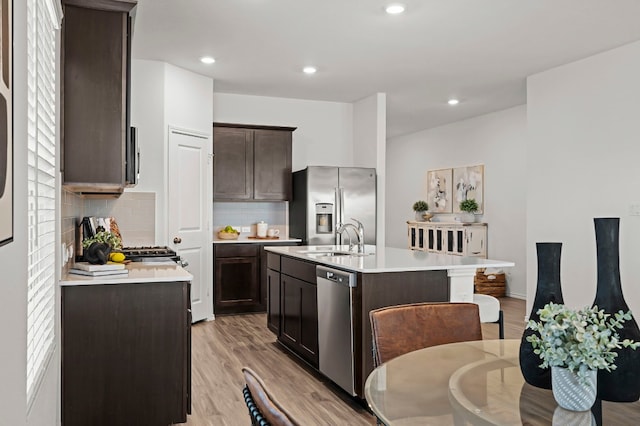 kitchen with sink, dark brown cabinets, light wood-type flooring, appliances with stainless steel finishes, and an island with sink