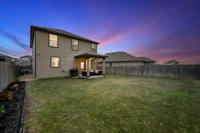 back house at dusk featuring a yard and a patio