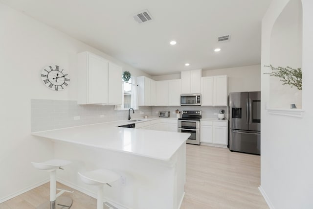 kitchen with tasteful backsplash, stainless steel appliances, kitchen peninsula, and white cabinets