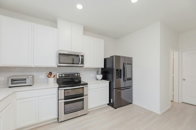 kitchen featuring white cabinetry, backsplash, light wood-type flooring, and appliances with stainless steel finishes