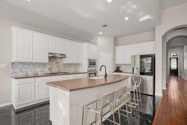 kitchen with a breakfast bar, white cabinetry, tasteful backsplash, a center island with sink, and appliances with stainless steel finishes