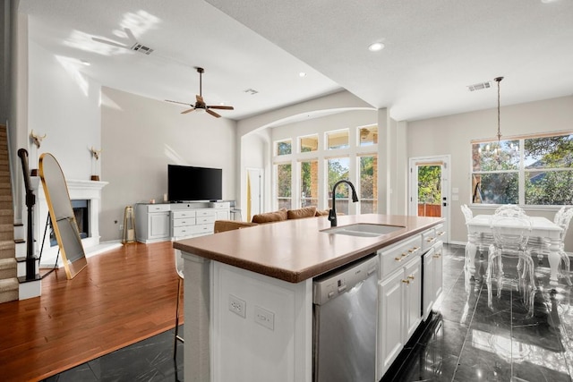 kitchen with a wealth of natural light, white cabinetry, an island with sink, sink, and stainless steel dishwasher