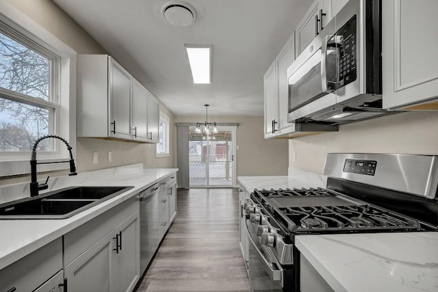 kitchen with appliances with stainless steel finishes, pendant lighting, white cabinetry, sink, and dark hardwood / wood-style flooring