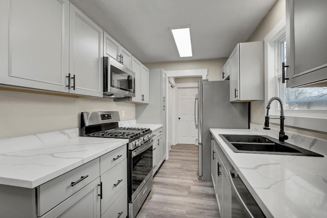 kitchen with sink, light hardwood / wood-style flooring, appliances with stainless steel finishes, a skylight, and light stone counters