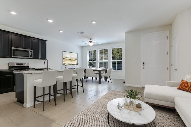 kitchen with decorative backsplash, a kitchen island with sink, light tile patterned floors, stainless steel appliances, and light stone countertops