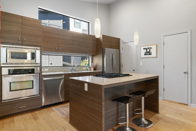 kitchen with sink, a center island, hanging light fixtures, stainless steel appliances, and a high ceiling