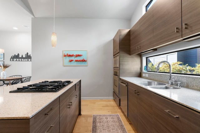 kitchen featuring sink, light hardwood / wood-style flooring, pendant lighting, stainless steel appliances, and light stone countertops