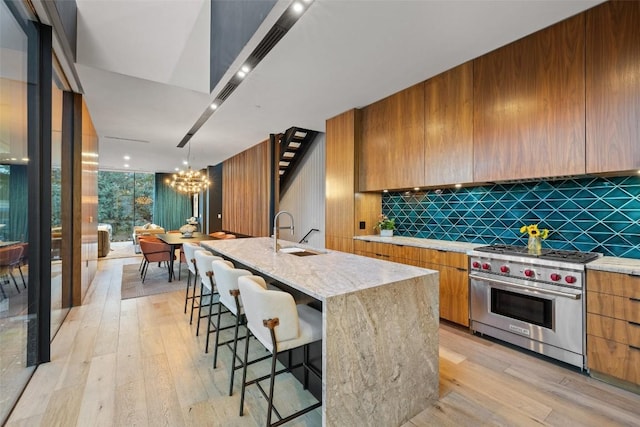 kitchen with pendant lighting, premium range, sink, a center island with sink, and decorative backsplash