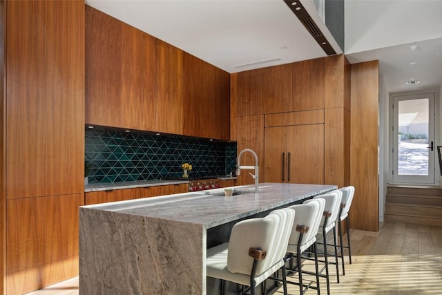 kitchen with sink, light hardwood / wood-style flooring, a kitchen breakfast bar, tasteful backsplash, and an island with sink