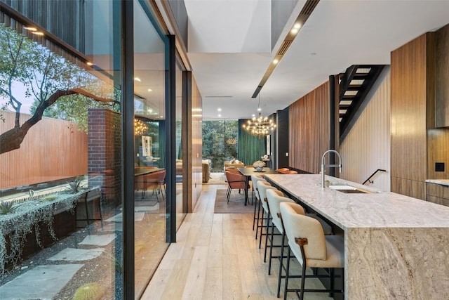 kitchen featuring sink, light hardwood / wood-style floors, expansive windows, decorative light fixtures, and a large island with sink