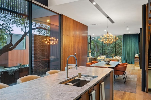 kitchen featuring an inviting chandelier, sink, light stone counters, and floor to ceiling windows