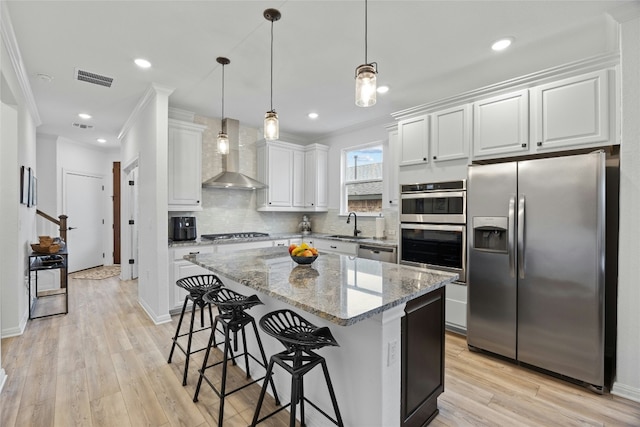 kitchen featuring white cabinetry, a center island, light stone counters, stainless steel appliances, and wall chimney exhaust hood