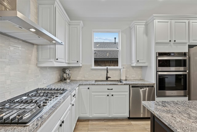 kitchen with wall chimney exhaust hood, sink, light stone counters, appliances with stainless steel finishes, and white cabinets