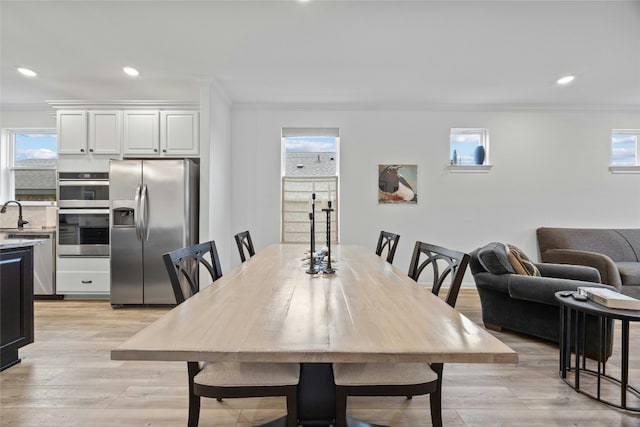 dining space with crown molding, sink, and light wood-type flooring