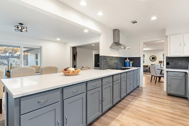 kitchen with black electric stovetop, gray cabinetry, light wood-style floors, light countertops, and wall chimney range hood