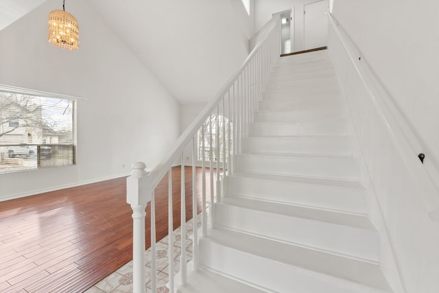 stairs with hardwood / wood-style flooring, a chandelier, and high vaulted ceiling