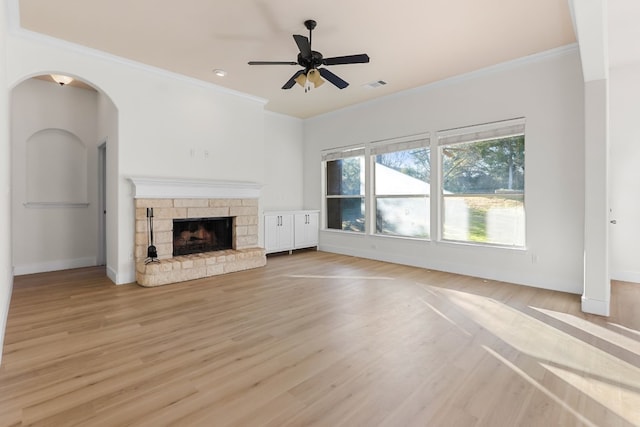 unfurnished living room with crown molding, ceiling fan, a stone fireplace, and light hardwood / wood-style flooring