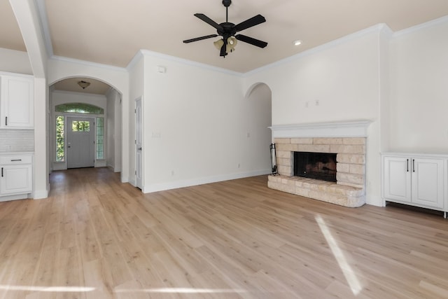 unfurnished living room featuring crown molding, ceiling fan, a stone fireplace, and light hardwood / wood-style flooring