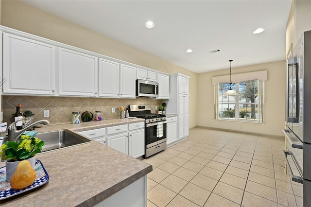 kitchen with appliances with stainless steel finishes, white cabinetry, sink, decorative backsplash, and hanging light fixtures