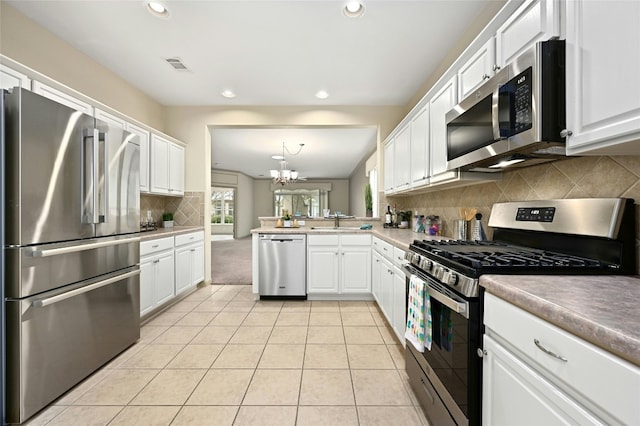 kitchen with appliances with stainless steel finishes, white cabinets, light tile patterned flooring, decorative light fixtures, and kitchen peninsula