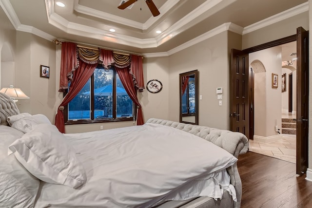 bedroom with dark wood-type flooring, connected bathroom, ornamental molding, a tray ceiling, and ceiling fan