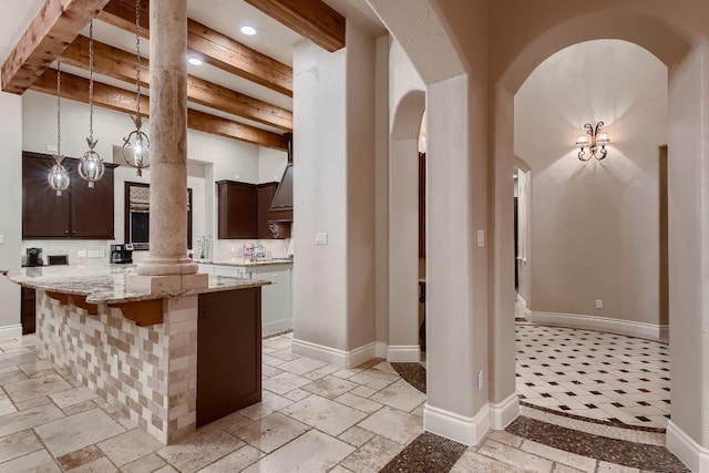 kitchen featuring beamed ceiling, light stone countertops, a center island, and dark brown cabinetry