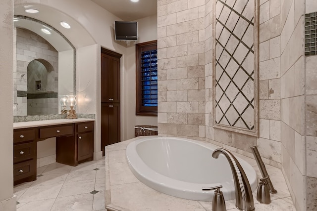 bathroom featuring a relaxing tiled tub, vanity, and tile patterned floors