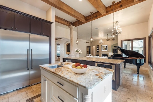 303 Camino Arbolago St, Lakeway, TX 78734 - kitchen featuring stainless steel built in fridge, arched walkways, stone tile flooring, an island with sink, and beamed ceiling