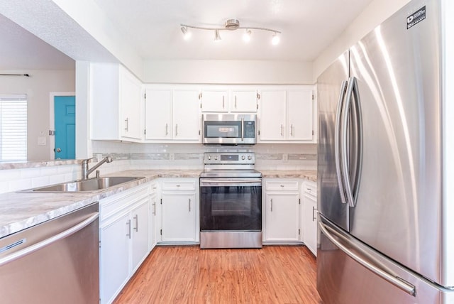 kitchen featuring sink, light hardwood / wood-style flooring, white cabinetry, stainless steel appliances, and decorative backsplash