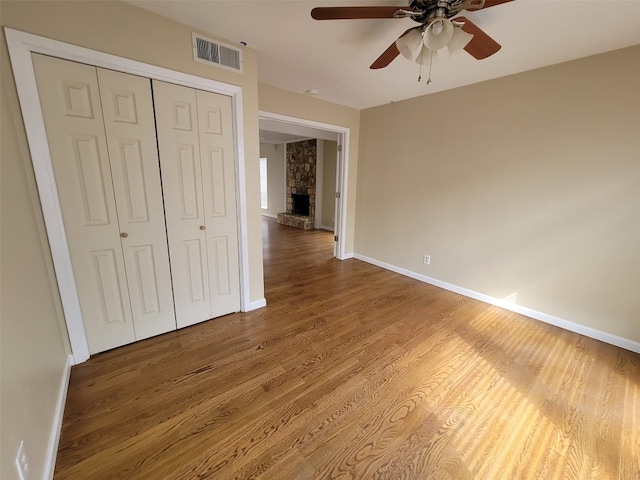 unfurnished bedroom featuring hardwood / wood-style flooring, ceiling fan, a stone fireplace, and a closet