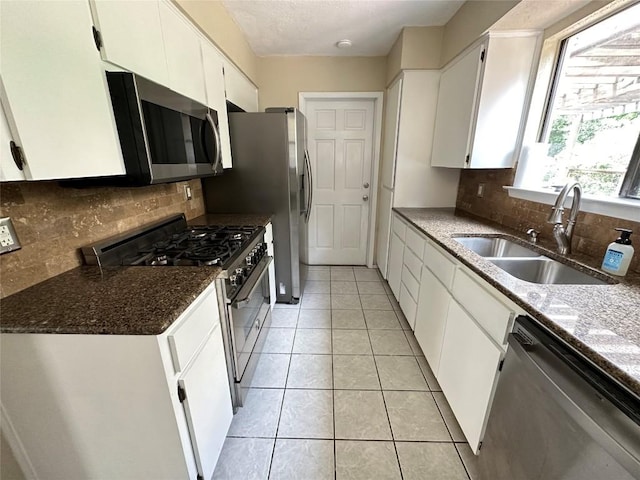 kitchen with sink, white cabinetry, light tile patterned floors, dark stone countertops, and stainless steel appliances