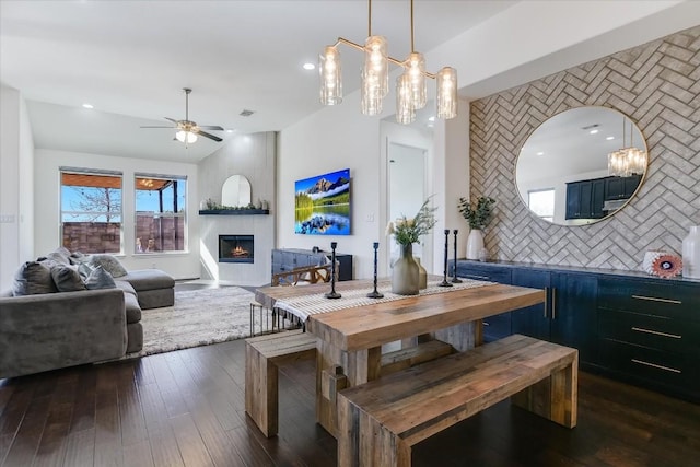 dining space with dark wood-type flooring, a large fireplace, ceiling fan, and vaulted ceiling