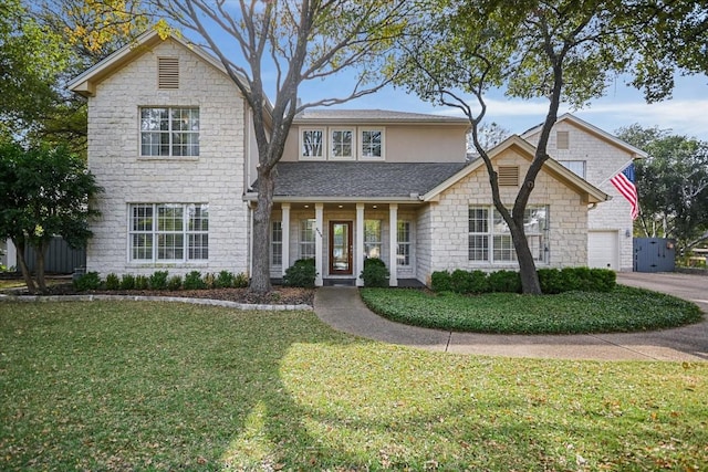 traditional home with a garage, a front yard, stone siding, a shingled roof, and driveway
