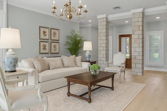 living area featuring visible vents, crown molding, decorative columns, an inviting chandelier, and light wood-style floors