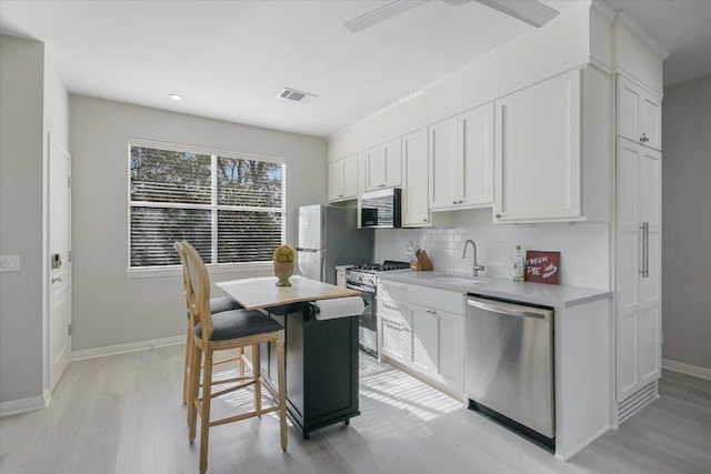 kitchen featuring visible vents, light wood-style floors, a sink, backsplash, and stainless steel appliances