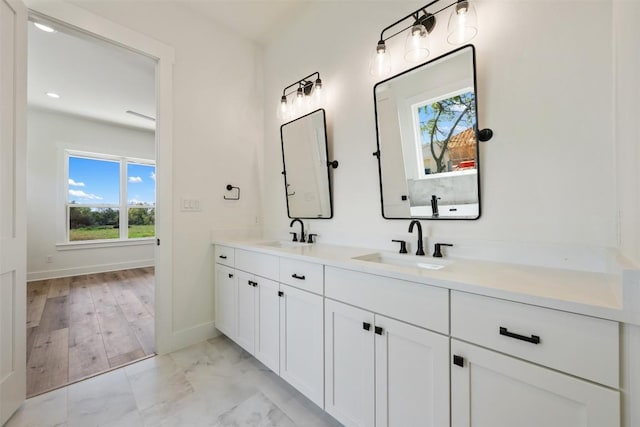 full bathroom with double vanity, marble finish floor, baseboards, and a sink