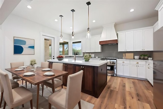 kitchen with a center island with sink, light countertops, hanging light fixtures, custom range hood, and high end range