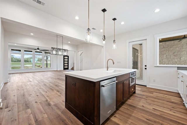 kitchen featuring a center island with sink, decorative light fixtures, stainless steel appliances, light countertops, and a sink