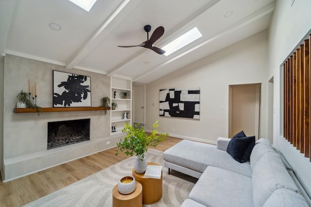 living room featuring ceiling fan, vaulted ceiling with skylight, a fireplace, and light hardwood / wood-style floors