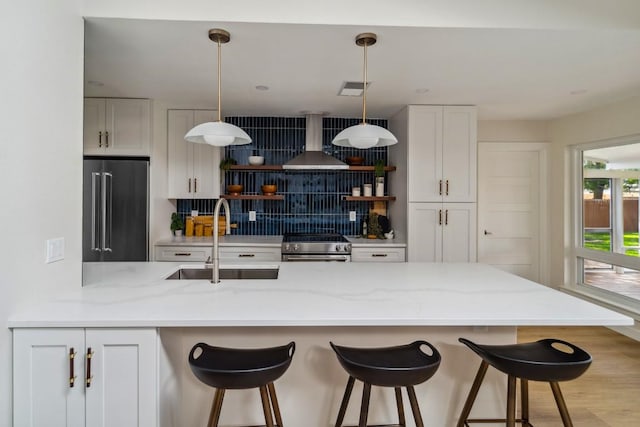 kitchen featuring wall chimney range hood, stainless steel appliances, sink, and white cabinets